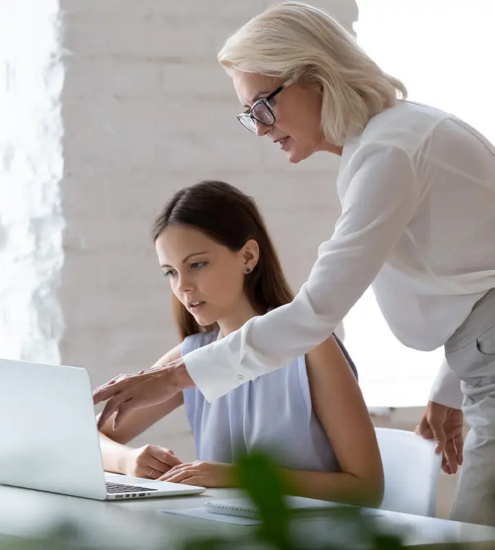 An employee shows her female colleague something on her laptop