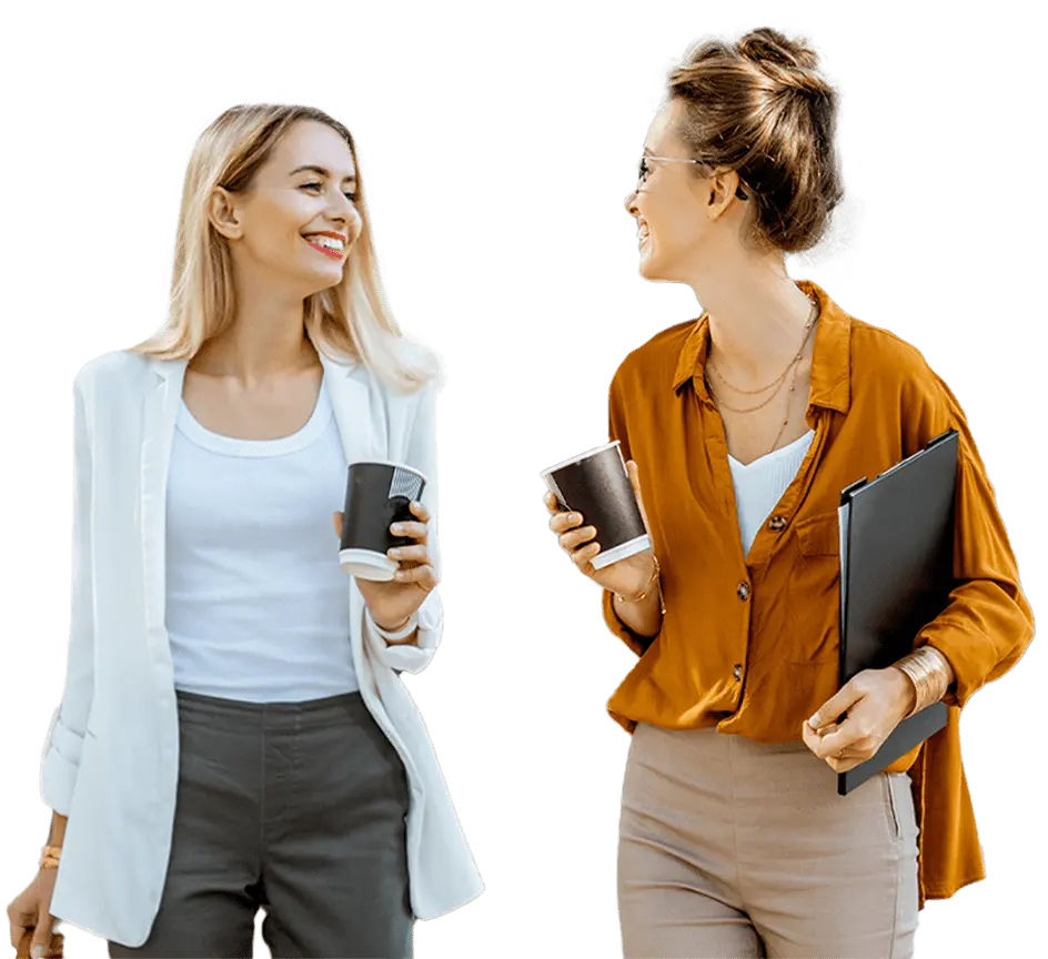 Female employees looking at each other smiling with coffee cups in hand